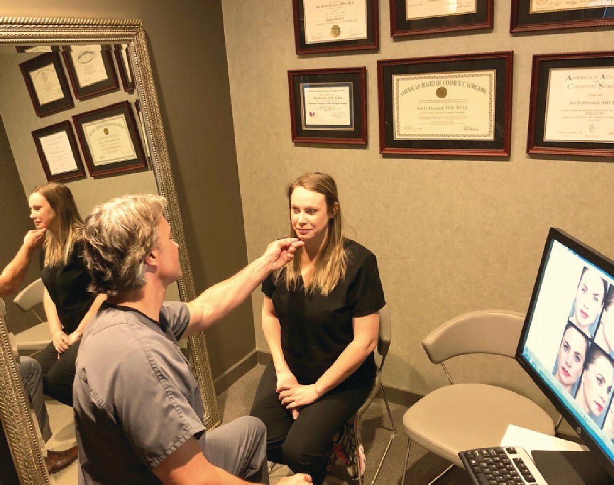 Photo of a consult room depicting a therapist sitting in front of a seated woman and touching her chin. At the right side of the woman is where a large mirror is located and at the left side is a computer for displaying multiple photos of a woman.