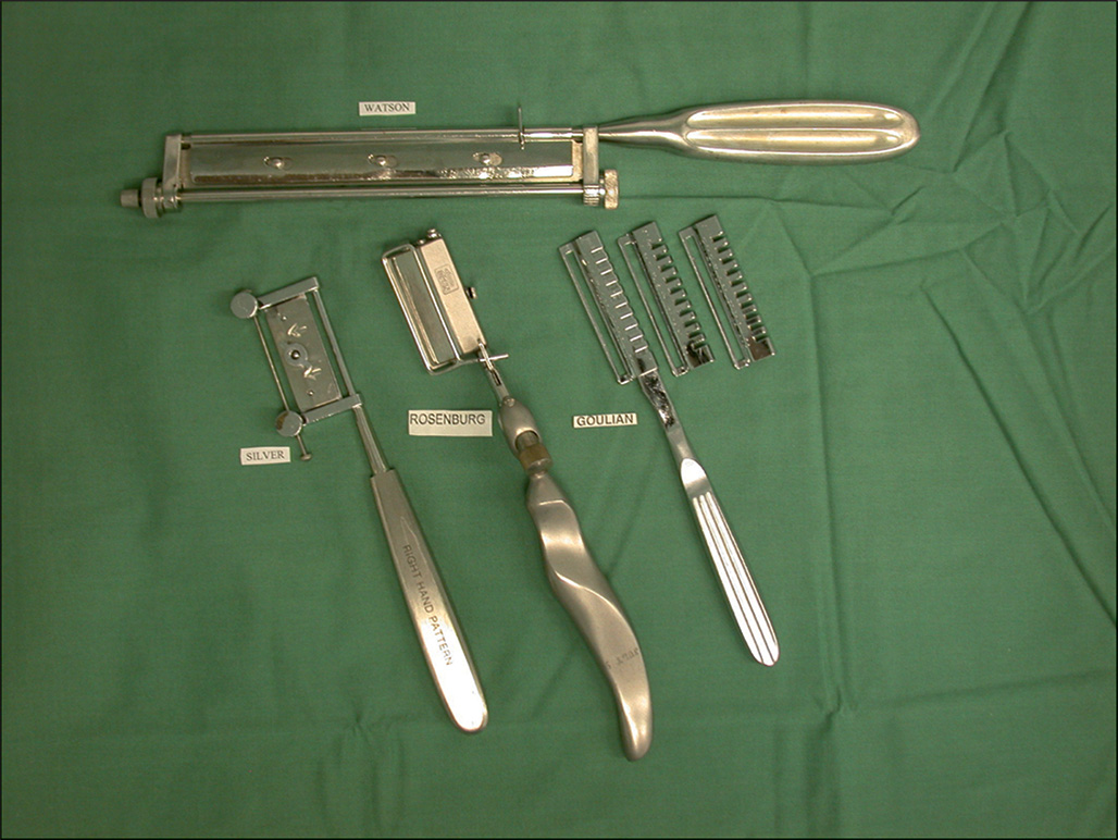 A capture of surgical instruments relatively humby skin grafting knife of four different types and two blades, placed on a surface, each labeled Watson, Silver, Rosenberg, and Goulian. The capture involves the metal surgical instruments arranged on a surface. All four instruments are of humby knives of four different types and sizes. The upper horizontal humby knife has an elongated, rectangular head connected to a wide, cylindrical handle. It is labeled with Watson. Below this, three instruments are arranged with two blades. On the left side, the instrument is the smallest, having a flat, rectangular head with screws and a slender, ribbed handle, and is labeled Silver. The middle instrument has a distinctively curved, ergonomic handle and a rectangular head with a blade, beneath a clasp, and the instrument is labeled Rosenberg. The right side instrument appears thin with a ribbed handle, two different sized blades, and is labeled Goulian.