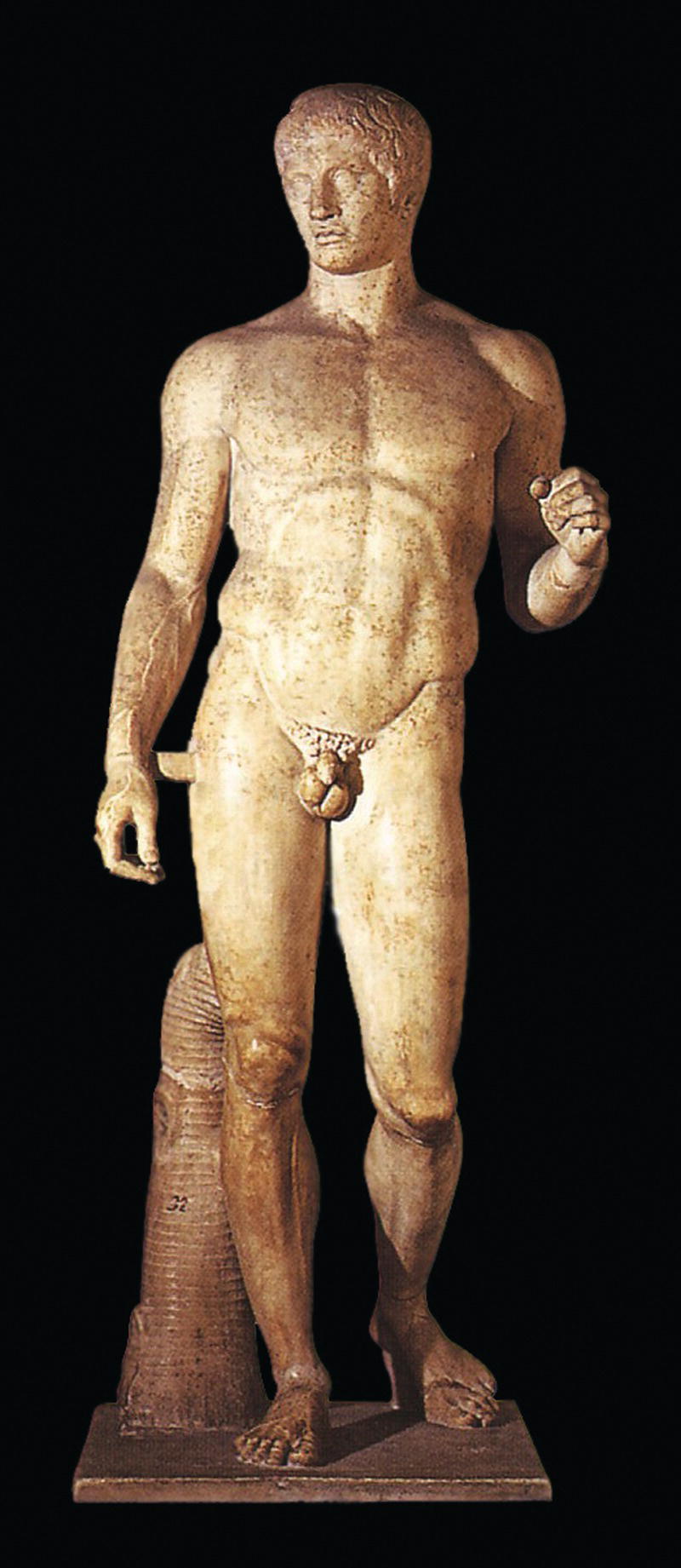 A statue of a male figure, standing in a contrapposto pose with detailed musculature. The figure holds an object in one hand, set against a black background.