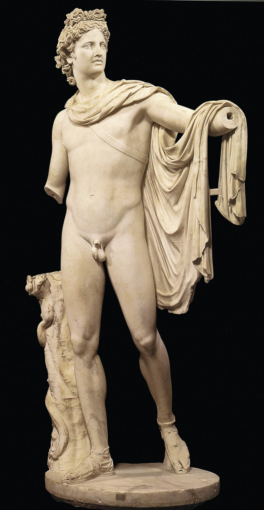 A statue of a male figure adorned with a draped cloak over one shoulder. The figure stands in a contrapposto pose with an ornate support column, set against a black background.
